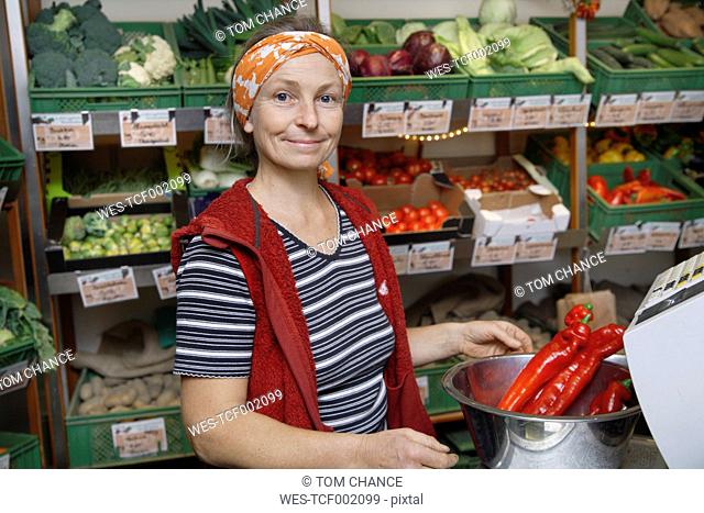 Germany, Upper Bavaria, Wolfratshausen, Mature woman with red chilli pepper in shop, smiling, portrait