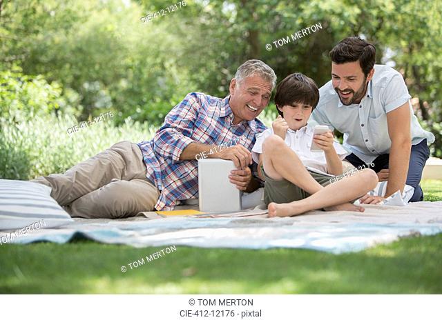 Multi-generation men with cell phone on blanket in grass