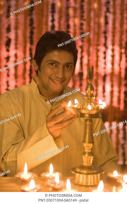 Portrait of a mid adult man lighting diwali lamps and smiling