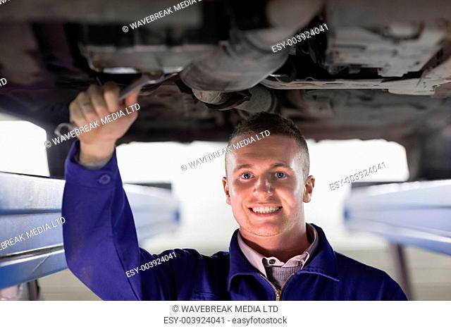 Smiling mechanic repairing a car with a spanner in a garage