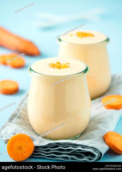 Yogurt with carrot. Vegetable yogurt. Two glass jar with yellow orange yoghurt or milkshake and fresh carrot on blue background. Copy space for text