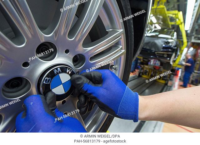 A staff member attaches the BMW logo to a wheel of a BMW car model at the assembly plant of car manufacturer BMW in Regensburg, Germany, 13 March 2015