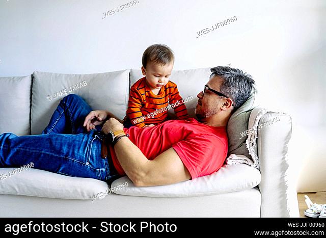 Father lying on sofa with son at home
