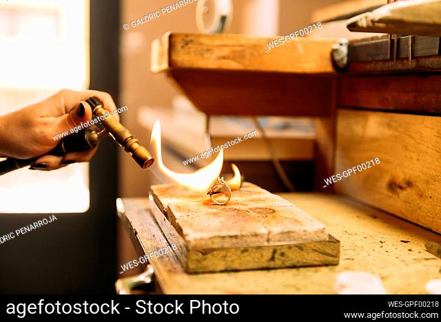 Female expert burning silver ring on wood at workshop