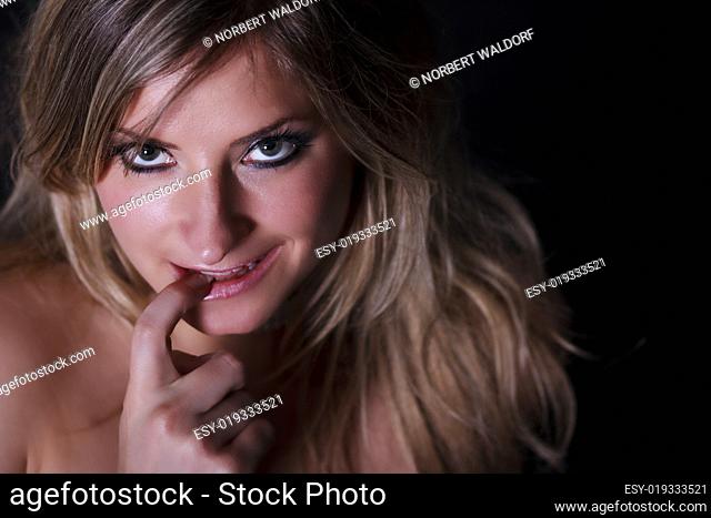Portrait einer jungen blonden Frau knabbert verschmitzt am Finger - direkter Bli