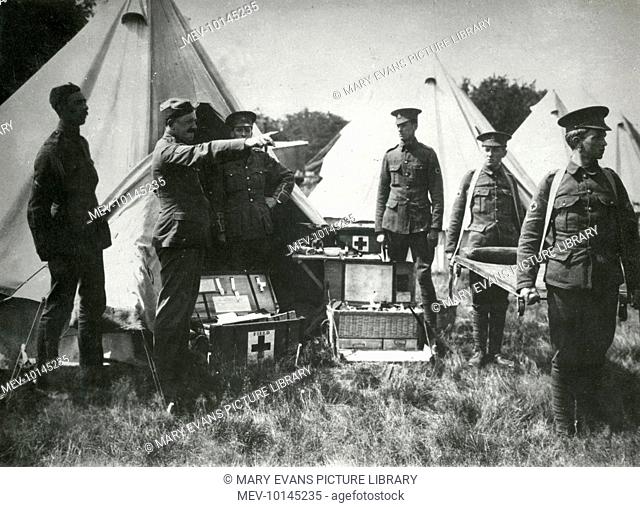 A British Red Cross encampment (field hospital) on the Western Front, showing baskets of medical supplies, soldiers carrying a stretcher and an officer giving...