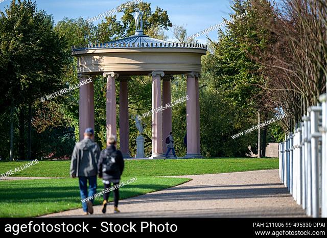 01 October 2021, Mecklenburg-Western Pomerania, Neustrelitz: Two strollers walk through the palace park. In the background is the Hebe temple with a copy of the...