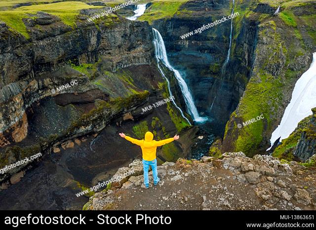 Aerial view of man in yellow jacket raise his hands up enjoying Icelandic highland valley and waterfall. Iceland