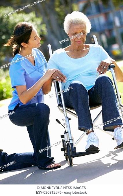 Carer Pushing Unhappy Senior Woman In Wheelchair