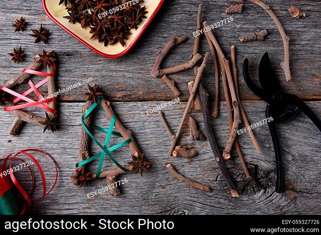 Top view of the equipment and supplies for making rustic Christmas decorations, including twigs, star anise, shears, and ribbon
