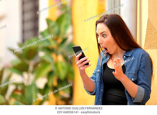 Surprised woman checking online news on smart phone in the street