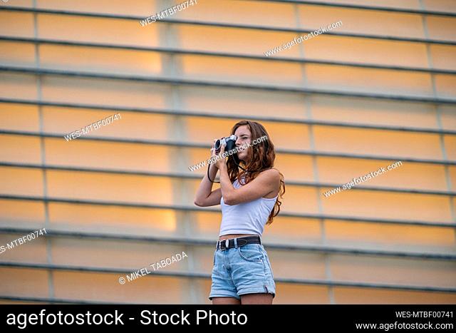 Woman taking photo through camera while standing against wall