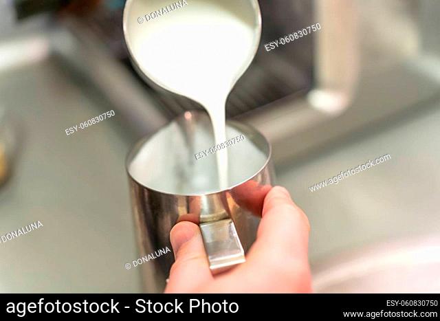 A barista pours whipped milk from one steel jug into another