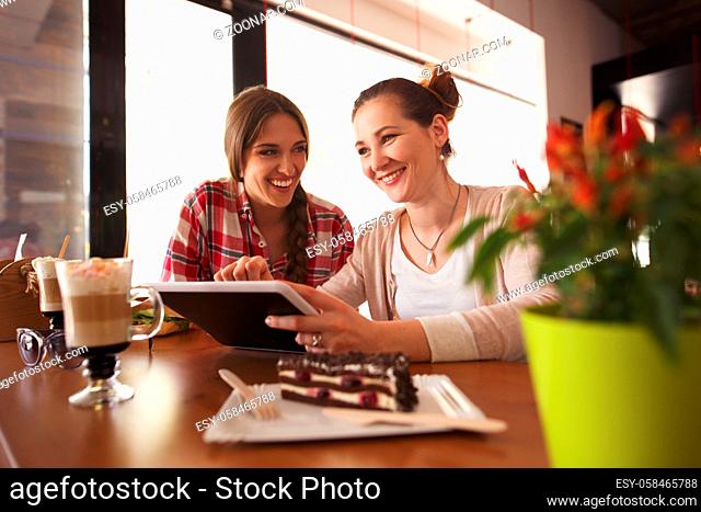 Toned picture of best friends discussing pictures or photos on tablet PC while sitting in cafe or restaurant. Weekends or break concept