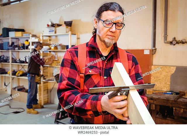 Carpenter looking if the wood plank is straight in his workshop
