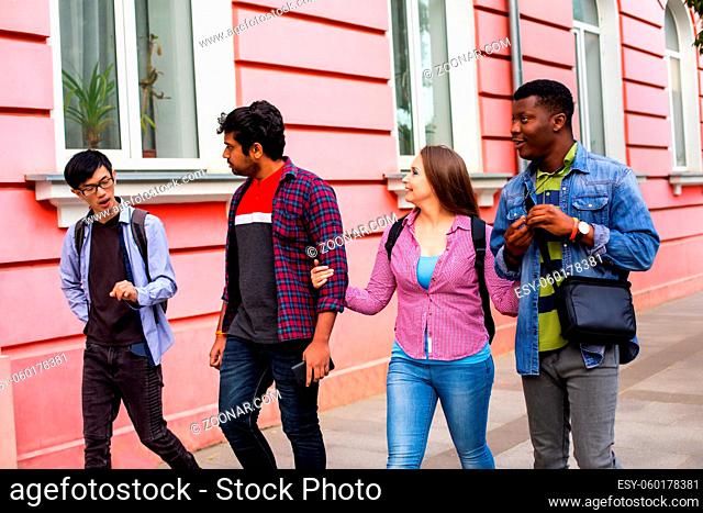 Four happy active young men and woman walking on street. Multiracial friends on the way shopping. Returning to normal life after lockdown