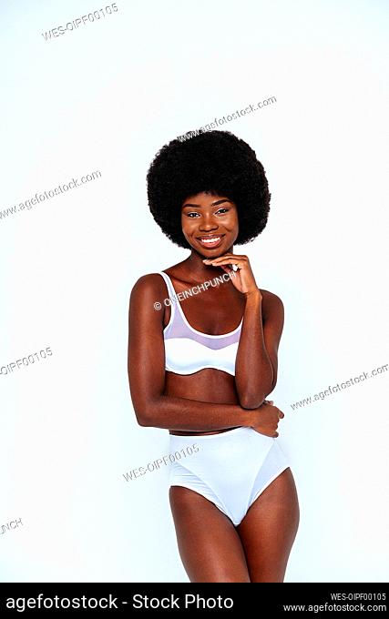 Skinny young woman with afro hair wearing lingerie standing against white background