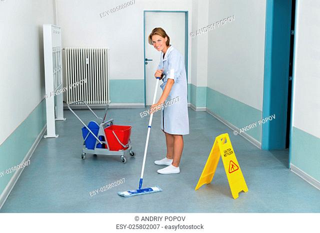 Young Female Janitor Mopping Floor With Wet Caution Sign And Cleaning Equipments