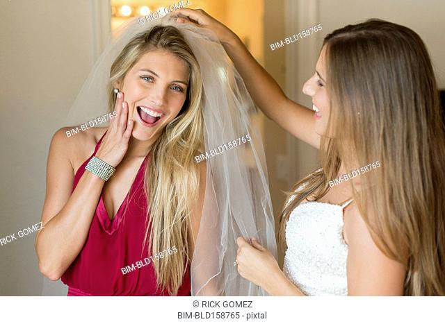 Caucasian bridesmaid wearing veil of bride
