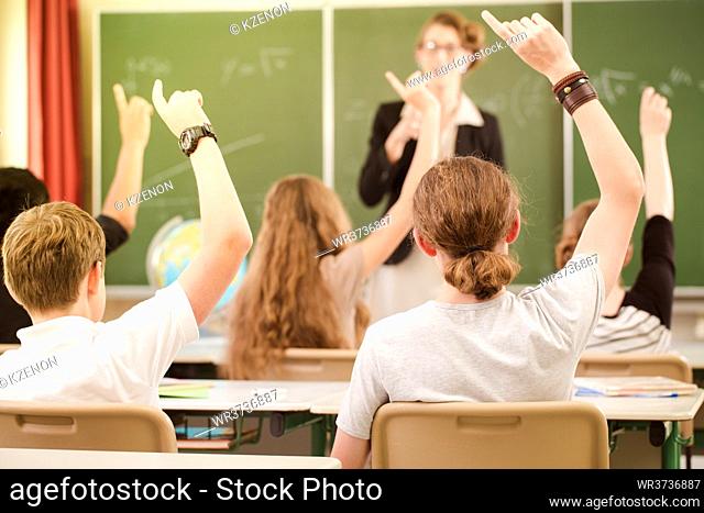 Teacher or docent standing while lesson in front of a blackboard or board and educate or teaching students or pupils or mates