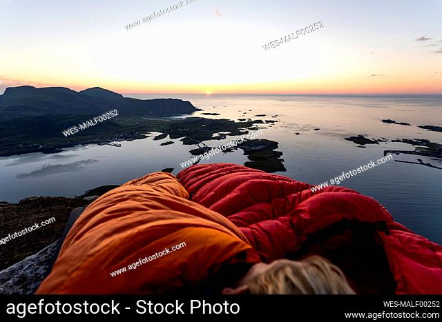 Hiker lying in sleeping bag against sea at Volandstinden, Lofoten, Norway