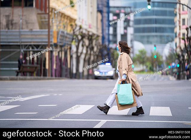 Woman crossing road with shopping bags during pandemic
