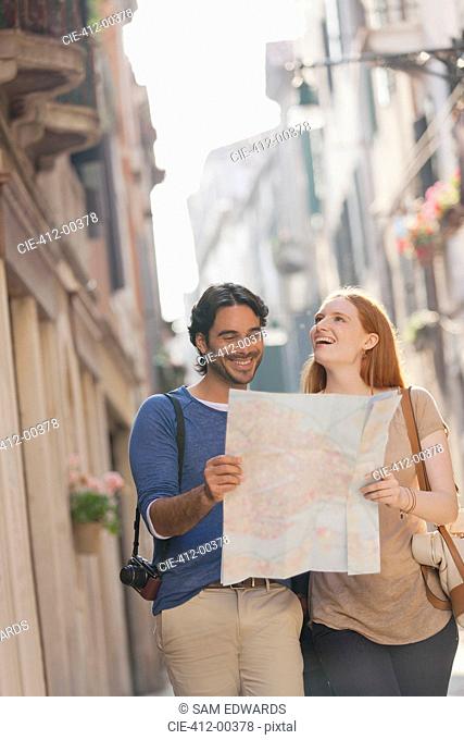 Smiling couple walking with map on narrow street in Venice
