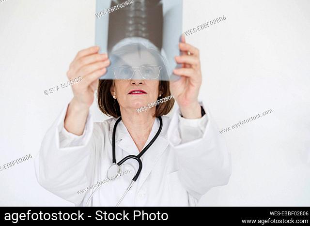 Senior female doctor examining x-ray image in front of white wall