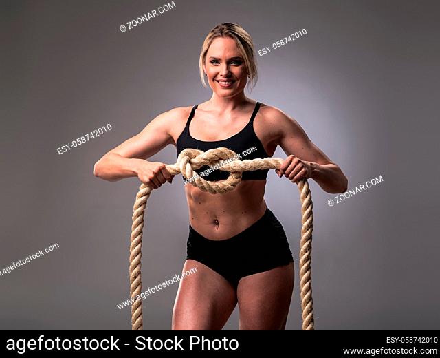 Attractive muscular woman holding node of heavy ropes on gray background