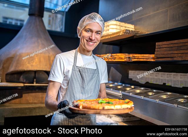 Bakery shop. A chef in apron and hair cap preparing pizza