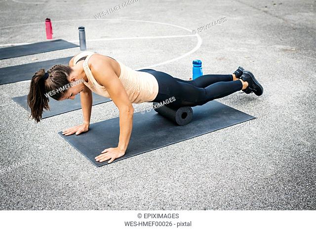 Young woman doing workout exercise with fascia roll outdoors