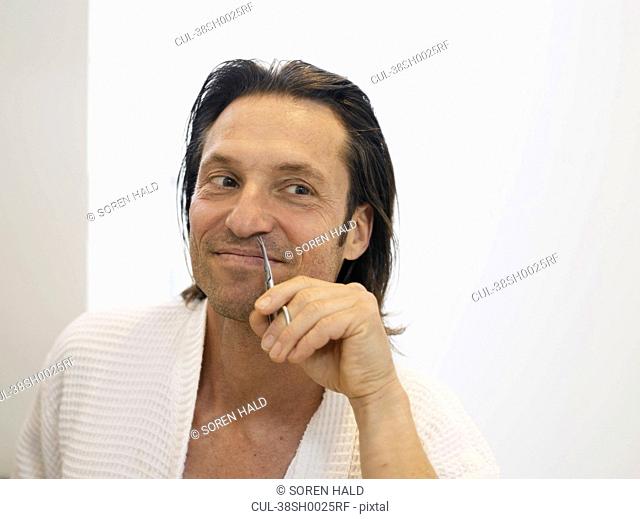 Smiling man clipping nose hairs