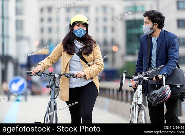 Business people in face masks walking bicycles on city bridge