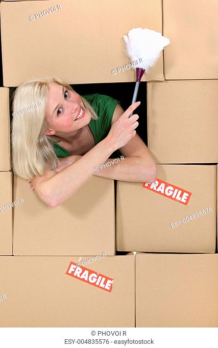 radiant blonde amid cardboard boxes holding feather duster