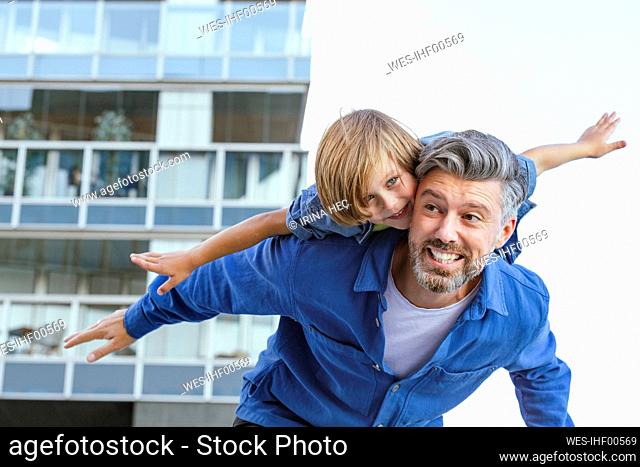 Playful man with arms outstretched piggybacking son