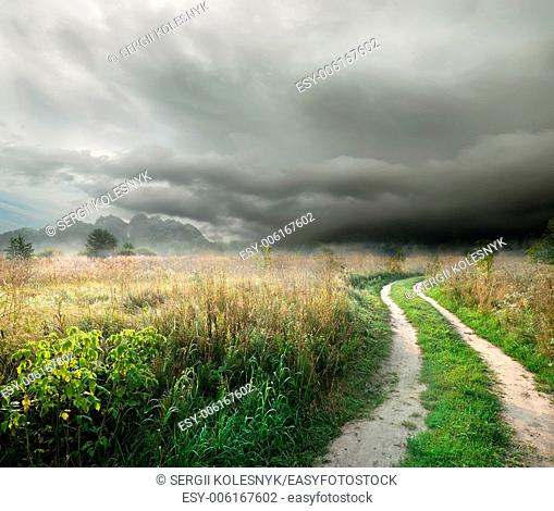 Country road in the field on a background of thunder clouds