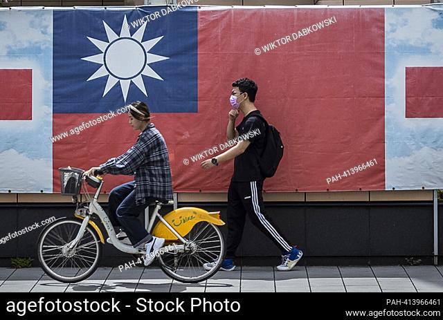 A woman riding a bicycle and a man on foot walk past a giant banner with the flag of the Republic of China in downtown in Taipei