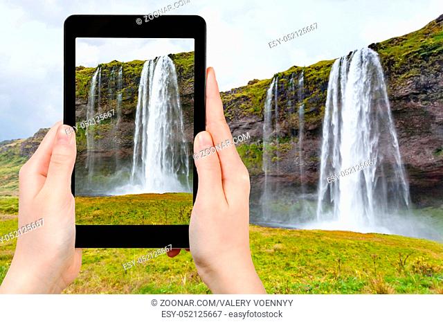 travel concept - tourist photographs Seljalandsfoss cascade of Seljalands River in Katla Geopark on Icelandic Atlantic South Coast in Iceland in september on...
