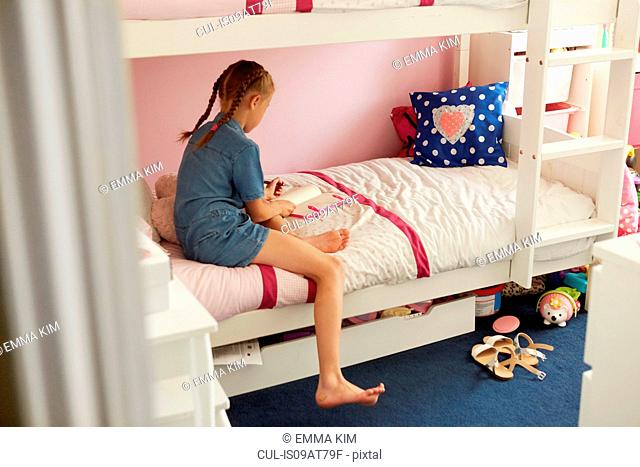 Rear view of girl sitting on bunkbed writing in notebook