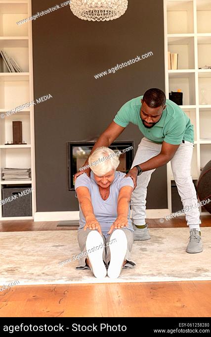 African american male physiotherapist helping caucasian senior woman to touch her toes wile sitting