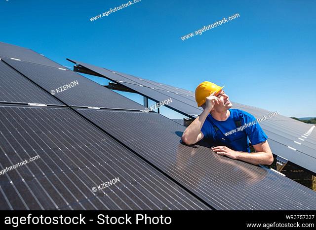 Maintenance worker with hardhat standing amid solar panels looking at sun