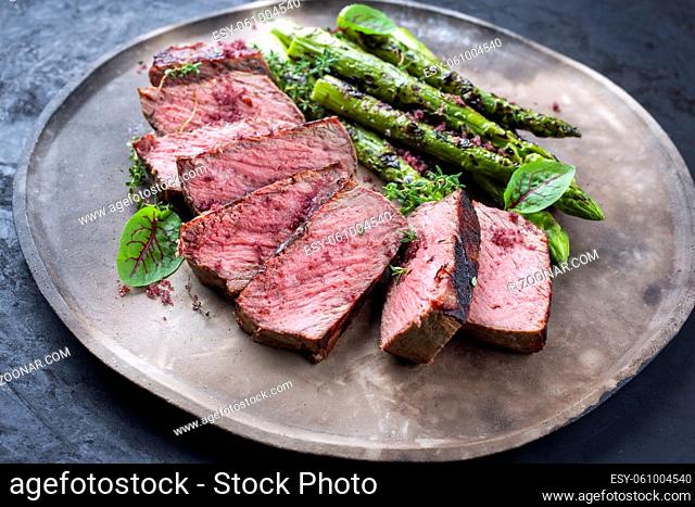 Barbecue dry aged wagyu roast beef steak with green asparagus and lettuce offered as close-up on a rustic modern design plate