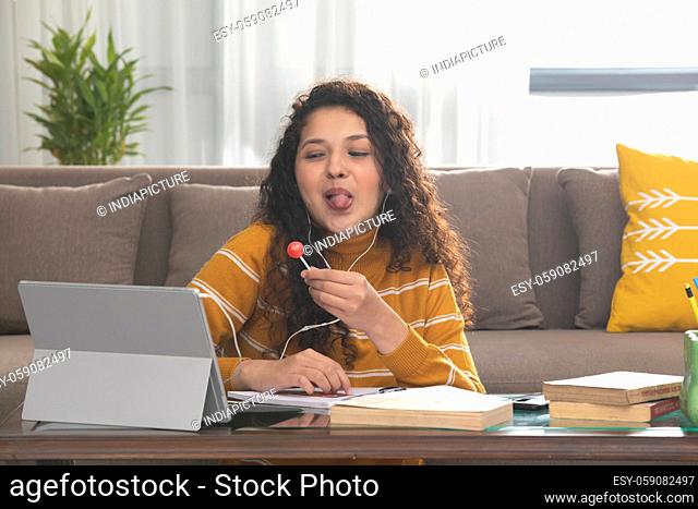 A TEENAGE GIRL EATING LOLLIPOP AND TEASING HER FRIENDS DURING ONLINE CLASS