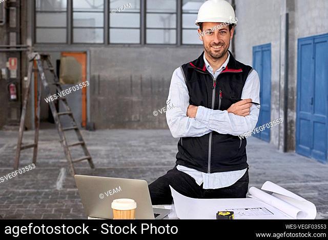 Confident male architect with arms crossed standing at table in building