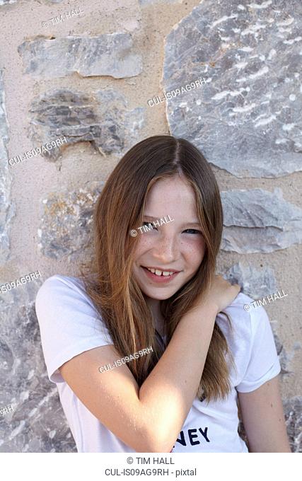 Portrait of shy smiling girl leaning against wall