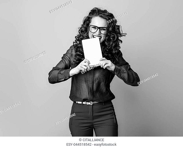 Portrait of smiling trendy woman with long wavy brunette hair biting tablet PC isolated on background