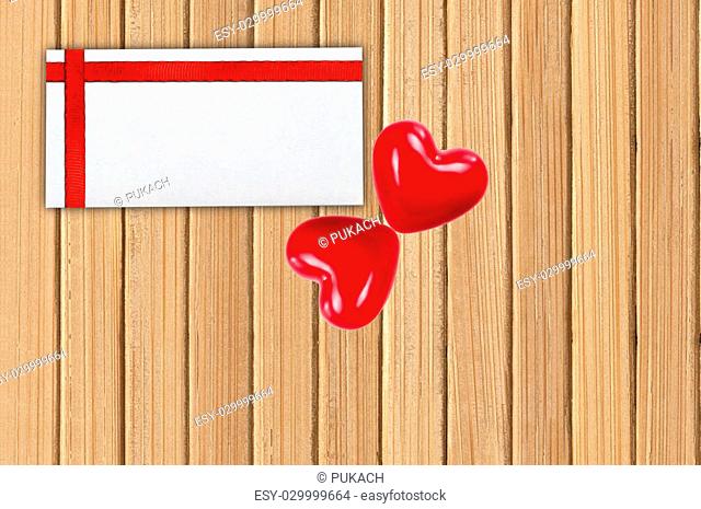 Greeting card with red ribbon and two red hearts on wooden planks background