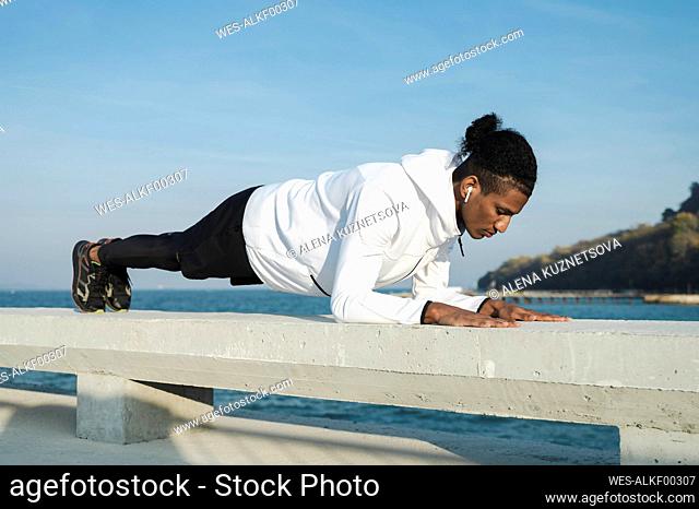 Athlete practicing plank position on railing at sunny day