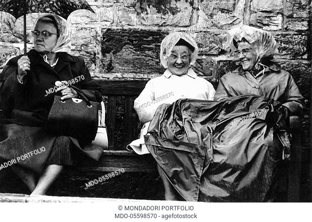 Three British elderly women sitting in the rain waiting for the sailing ship Gipsy Moth to come. Plymouth, May 1967