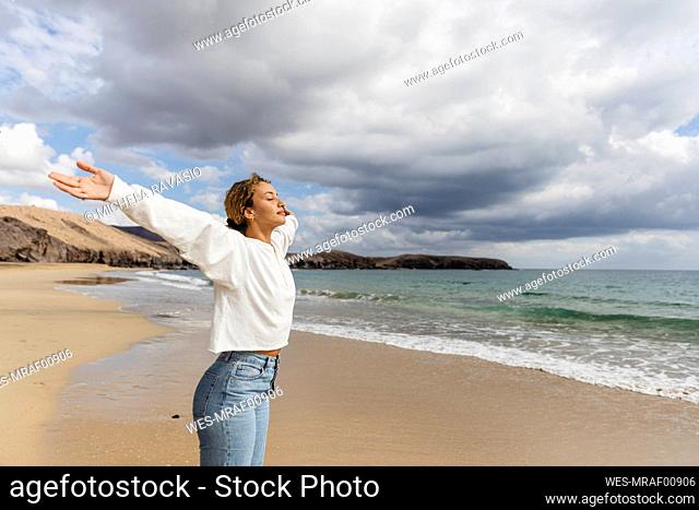 Young woman with arms outstretched and eyes closed enjoying sunny day at beach